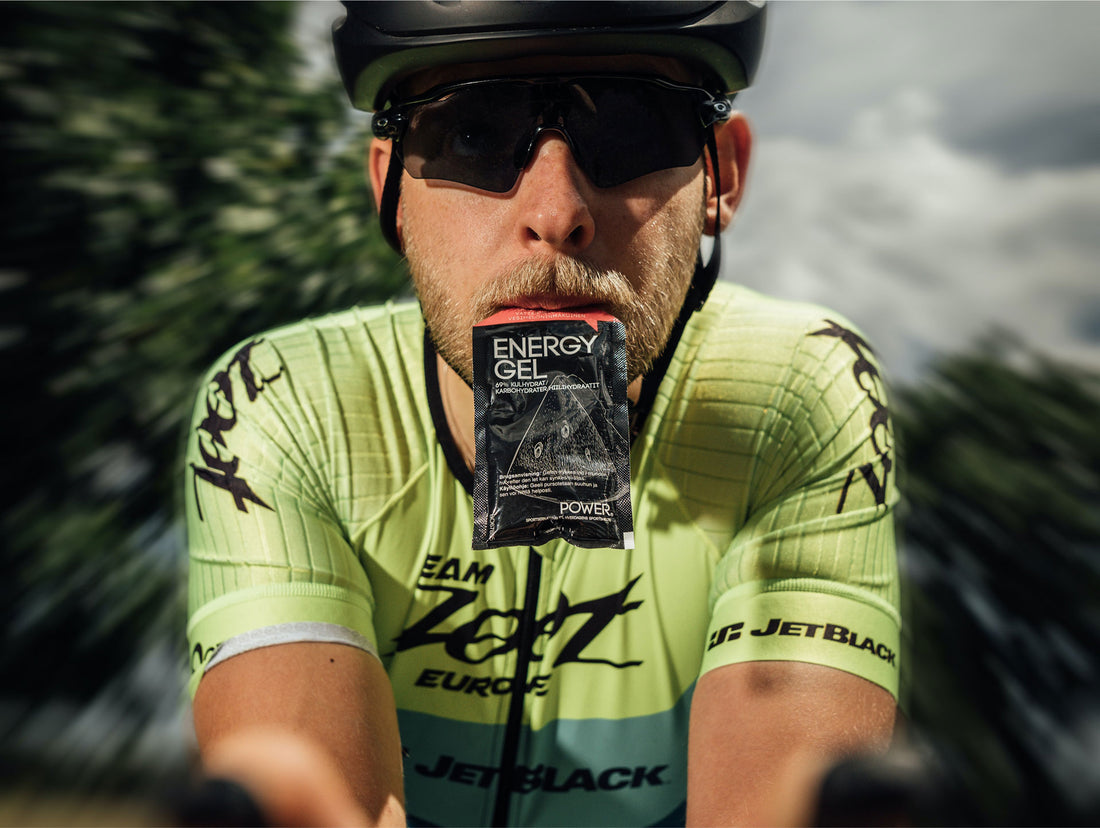 Ein Radfahrer in gelbem Trikot und Sonnenbrille hält ein Energiegel-Paket im Mund. Das Bild vermittelt Energie und Ausdauer bei sportlichen Aktivitäten.