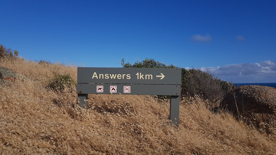 Ein Wegweiser in einer trockenen Graslandschaft mit der Aufschrift 'Answers 1km' und Pfeil nach rechts, begleitet von Symbolen, die Pferde, Feuer und Fahrräder verbieten.